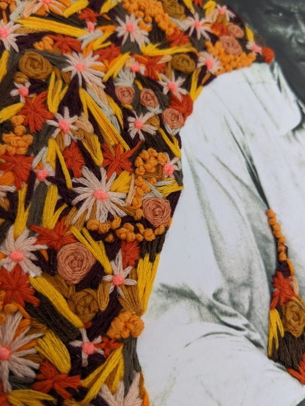 Detail of embroidery art of orange flowers on black and white photo of man sitting on steps